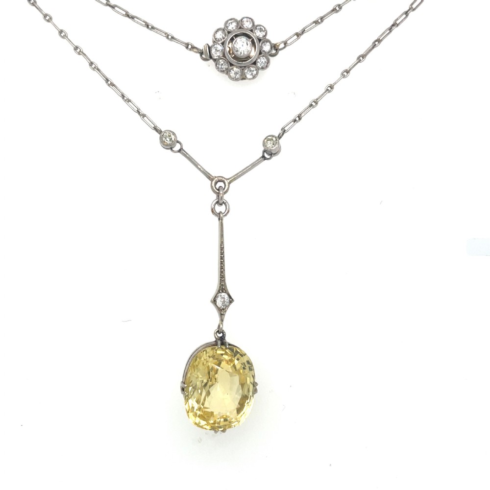 An Edwardian platinum pendant featuring an oval cushion-cut yellow sapphire suspended from a diamond-set drop chain. View VII