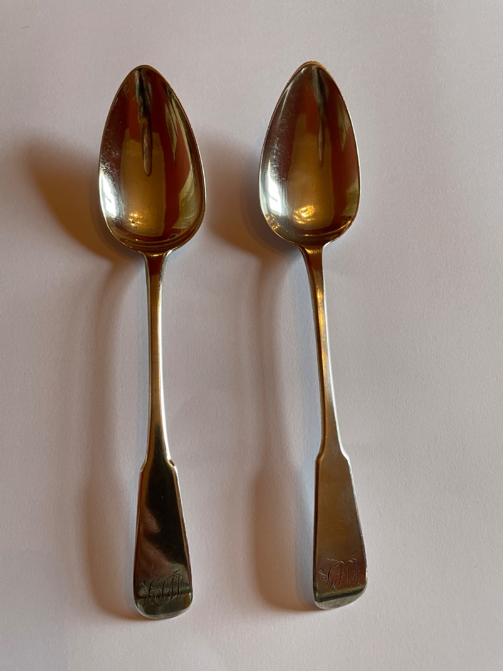 A pair of Georgian sterling silver serving spoons with smooth oval bowls and engraved monograms on the handles.