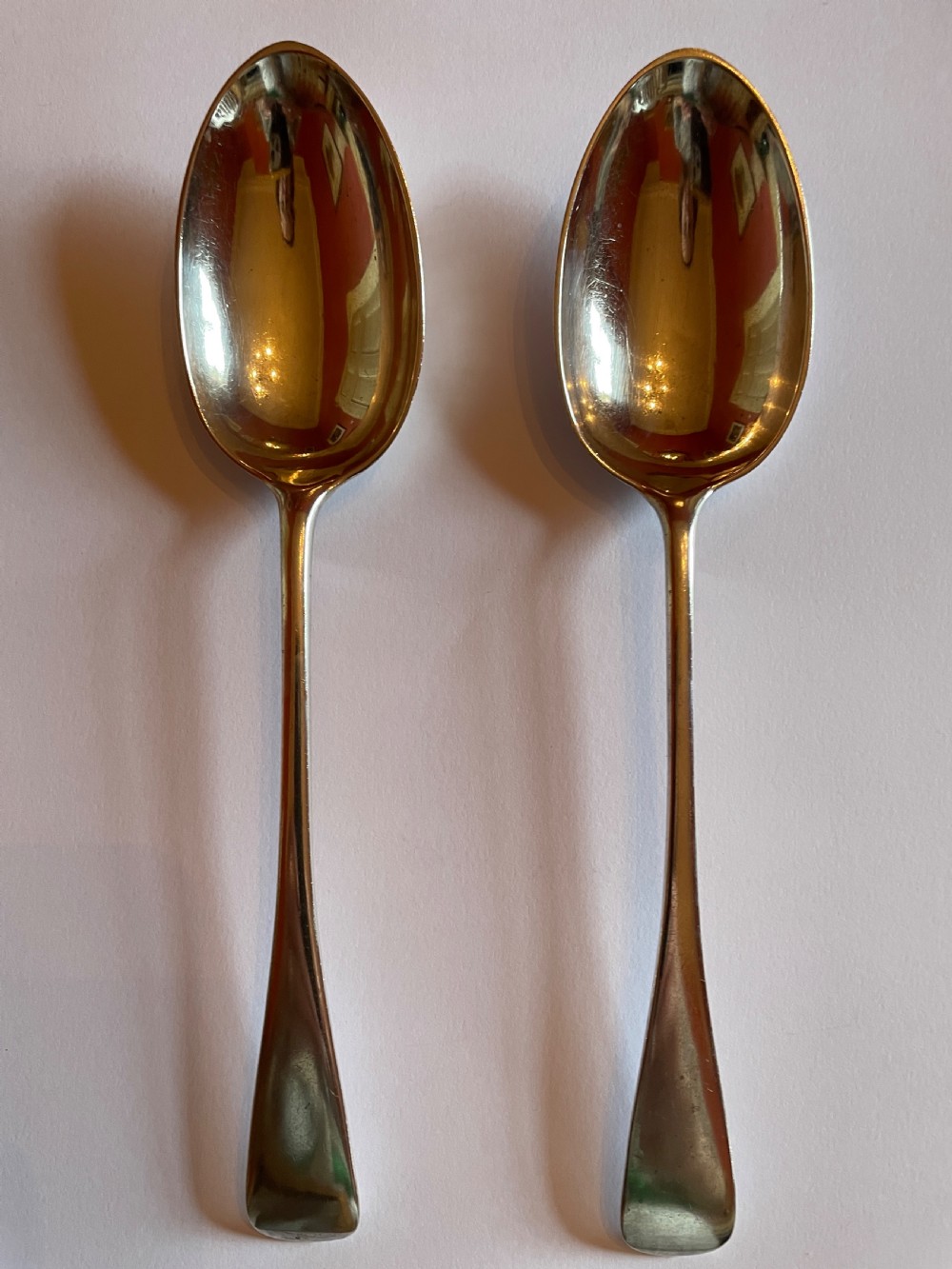 A pair of polished Georgian sterling silver serving spoons featuring elongated oval bowls and smooth tapered handles.