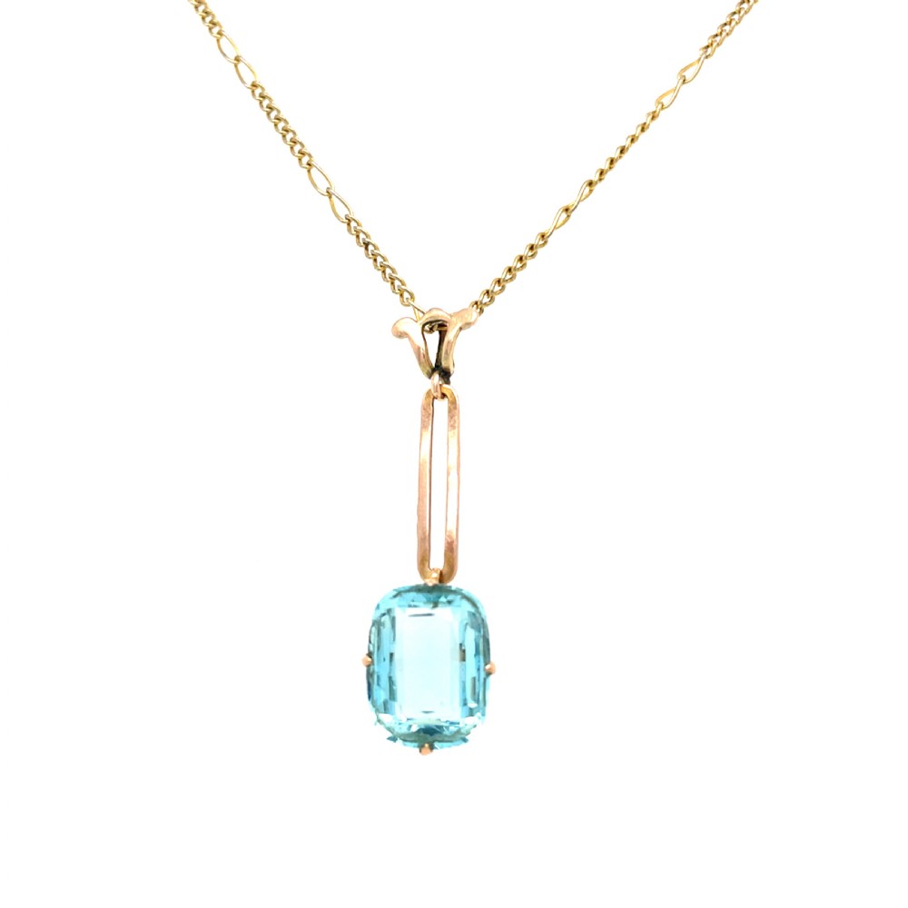 An Art Deco gold pendant featuring a rectangular step-cut light blue aquamarine gemstone suspended from an elongated gold link chain.