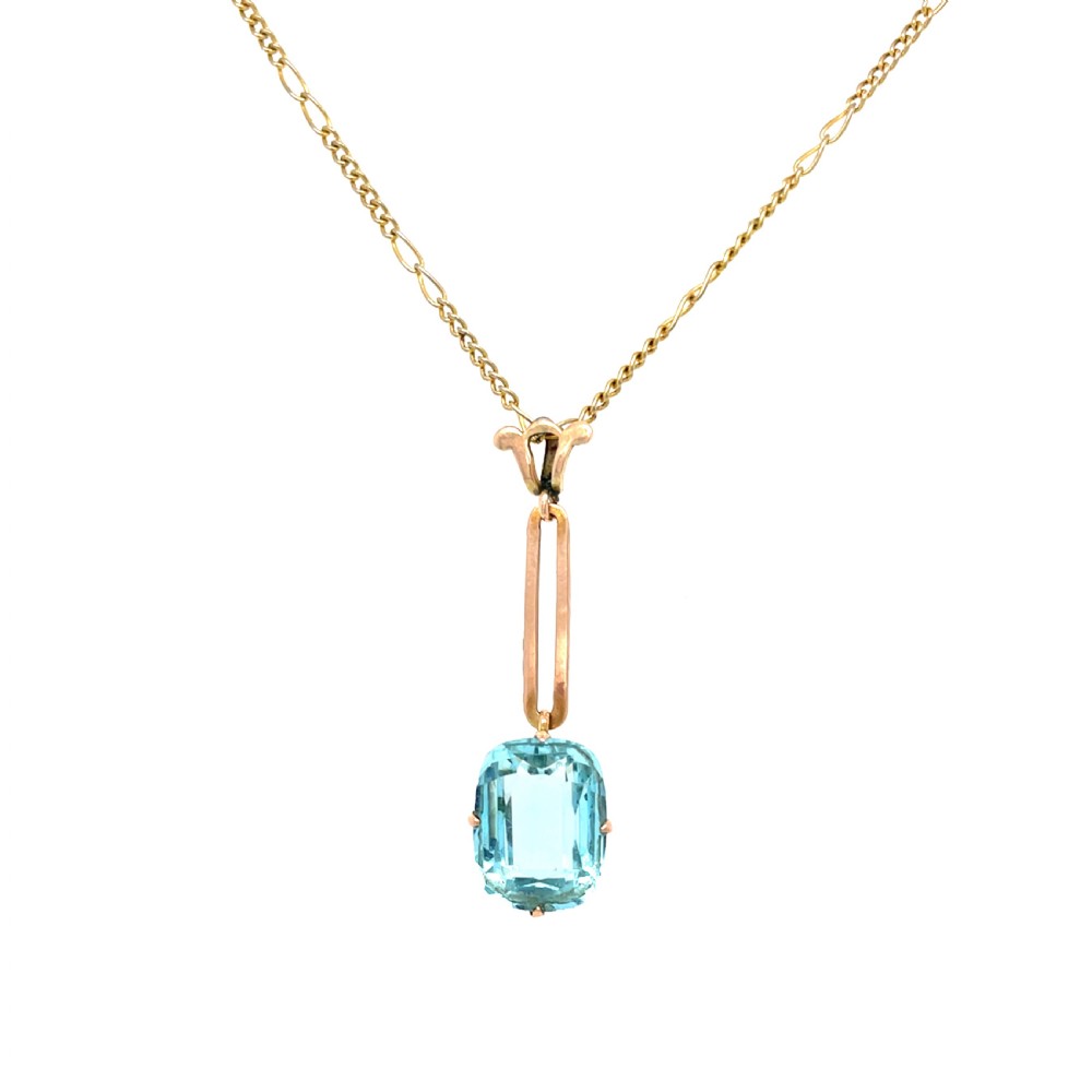 An Art Deco gold pendant featuring a rectangular step-cut light blue aquamarine gemstone suspended from an elongated gold link chain. View II