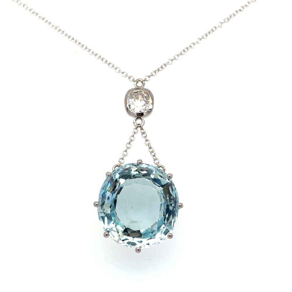 An antique 18ct white gold pendant featuring a faceted oval light blue aquamarine gemstone suspended beneath a single bezel-set diamond.