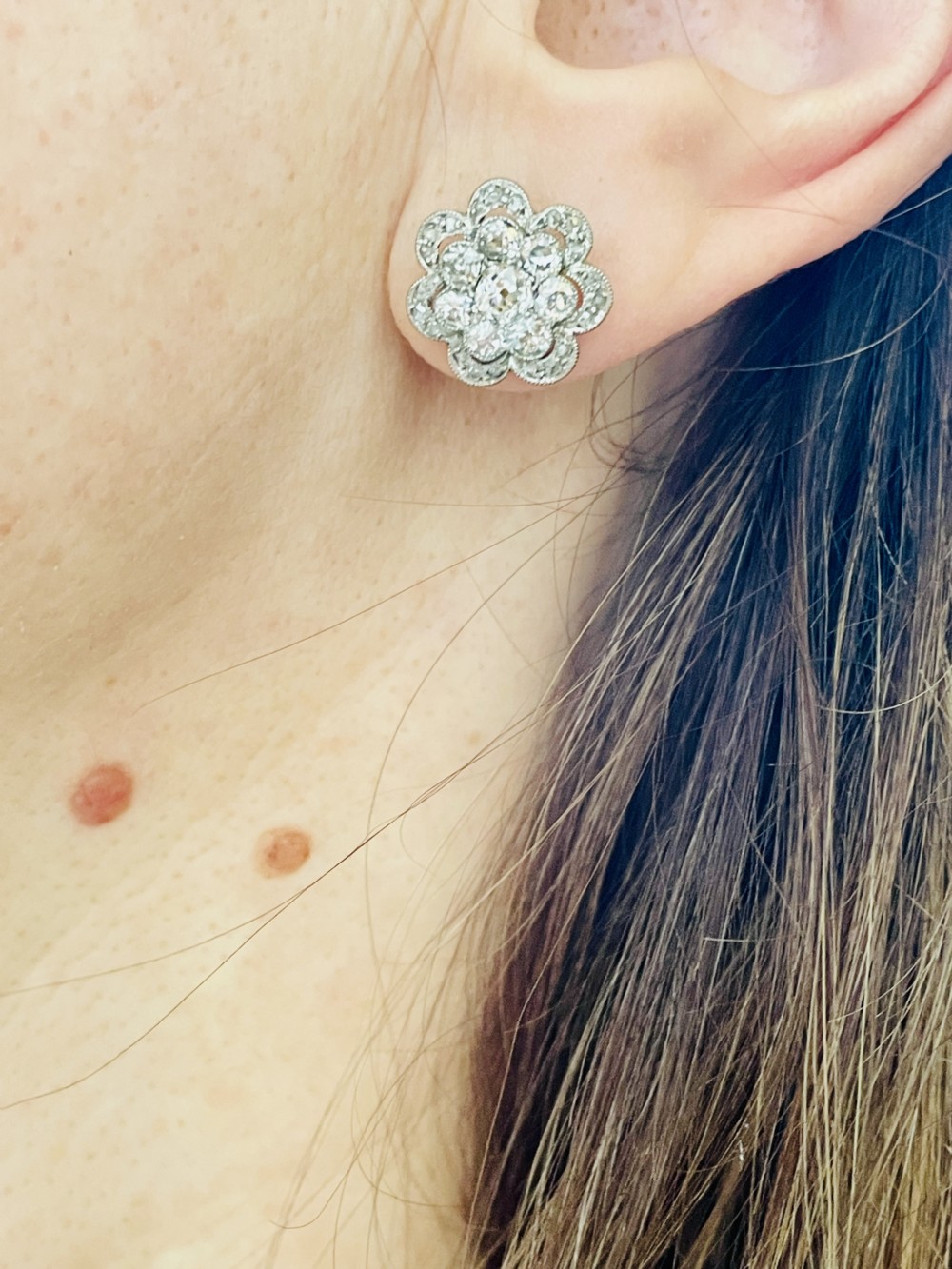 A pair of floral-shaped stud earrings set with central old European cut diamonds surrounded by millegrain-bordered diamond petals. View IV