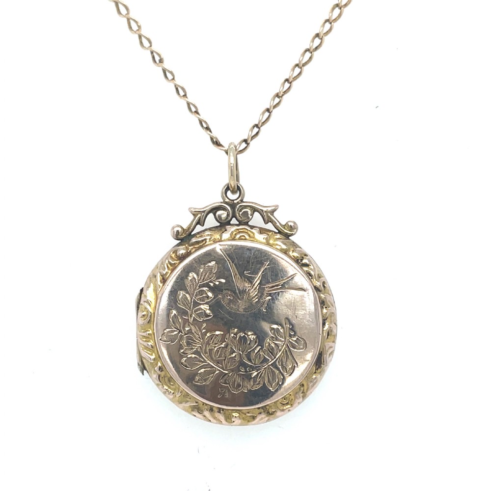 A round Edwardian gold locket engraved with a swallow in flight and floral foliage on a fine chain.