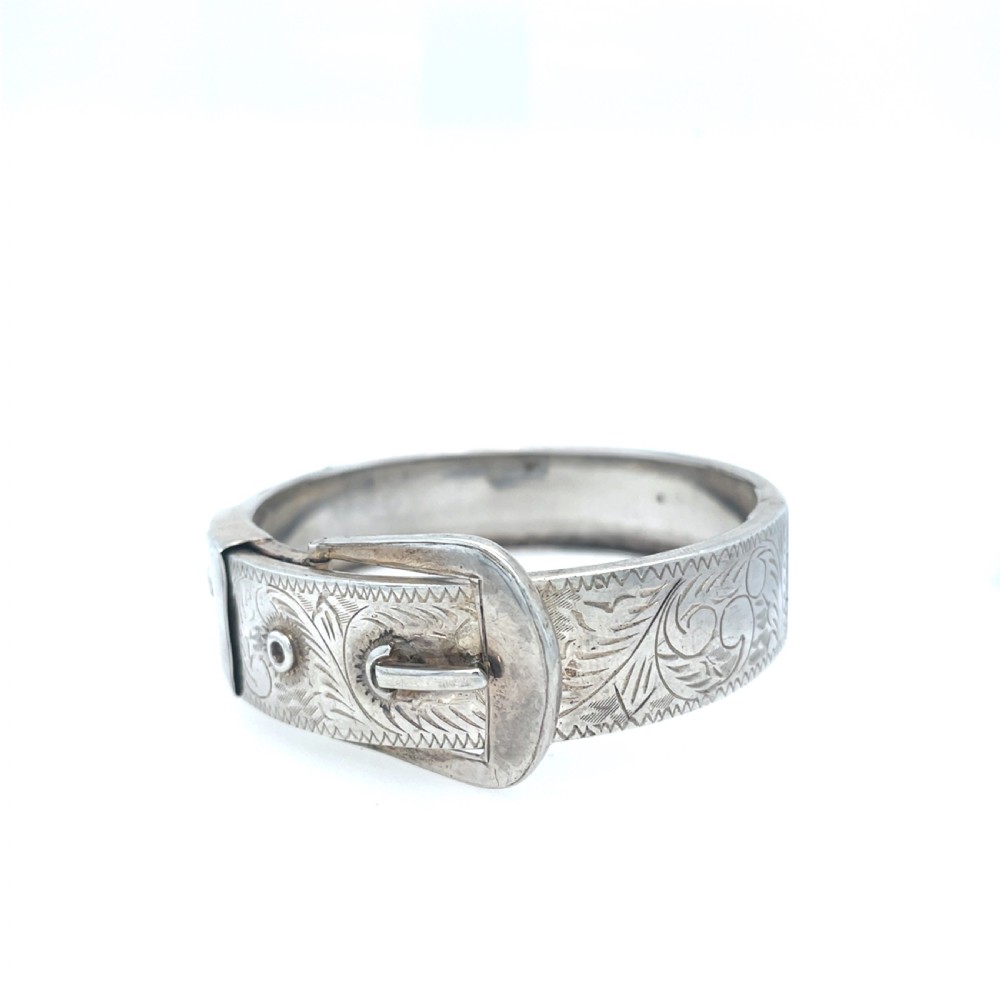 An engraved silver Victorian hinged bangle styled with a decorative buckle motif and foliate patterns.
