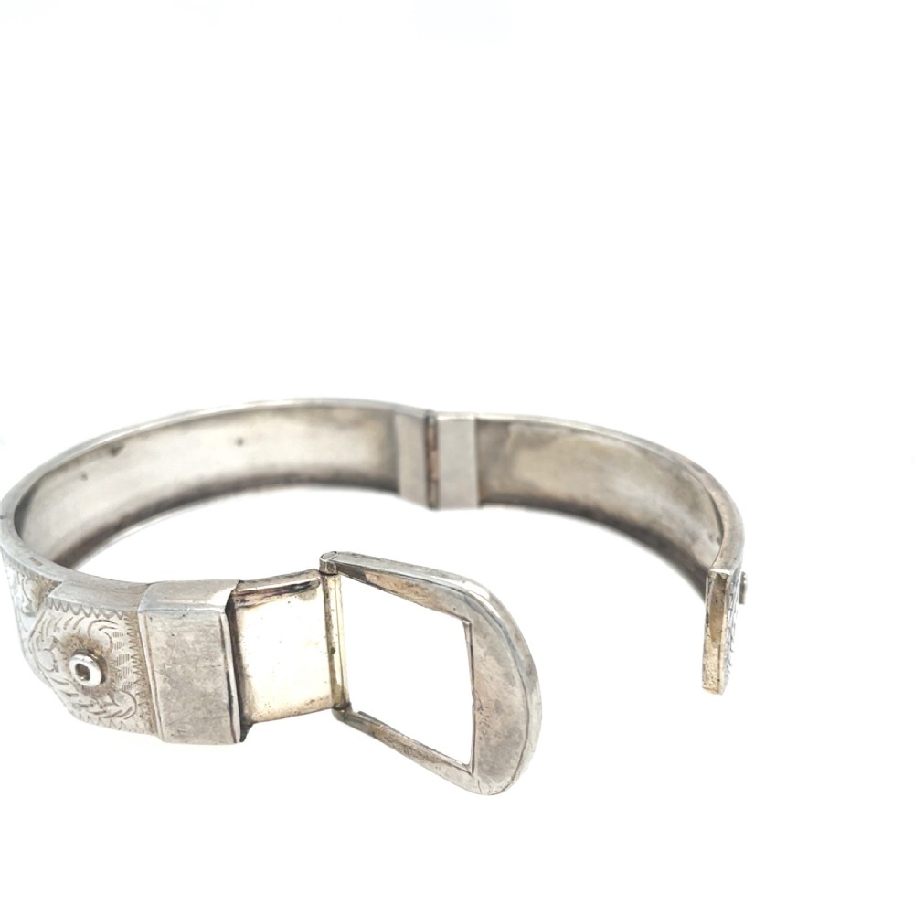 An engraved silver Victorian hinged bangle styled with a decorative buckle motif and foliate patterns. View II