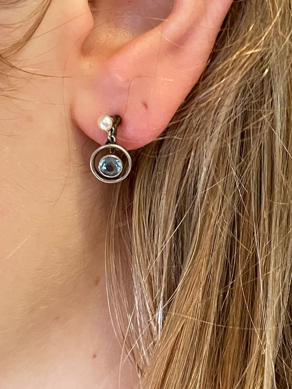 A pair of Edwardian drop earrings featuring round bezel-set aquamarine gemstones inside open circular mounts suspended from pearl studs. View IV