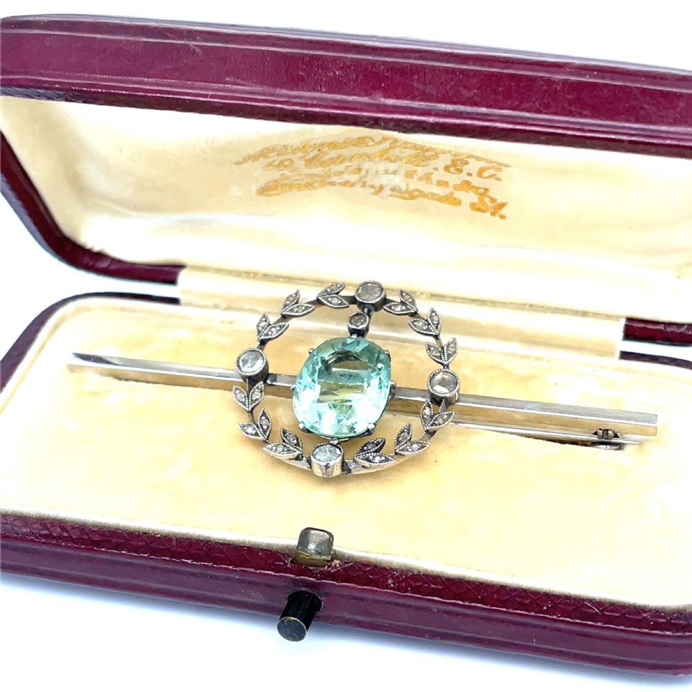 An Edwardian bar brooch featuring a central oval pale green aquamarine encircled by a diamond-set leaf wreath motif. View II