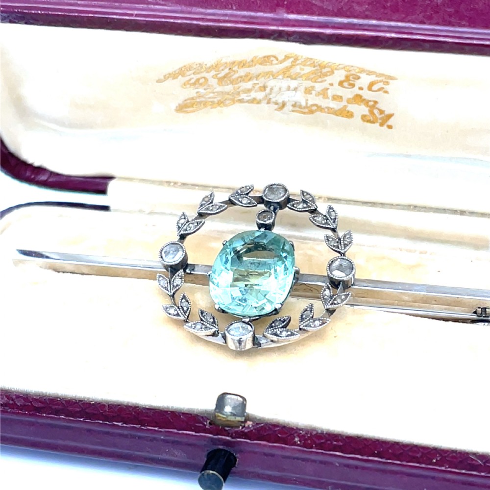 An Edwardian bar brooch featuring a central oval pale green aquamarine encircled by a diamond-set leaf wreath motif. View III
