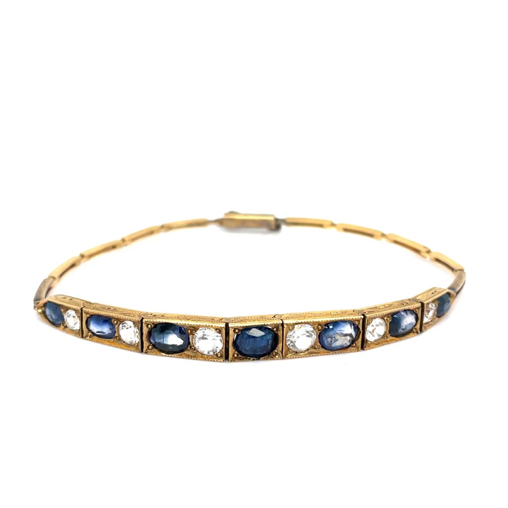 An Edwardian 9ct gold link bracelet featuring alternating set blue sapphires and clear round gemstones in articulated rectangular panels.