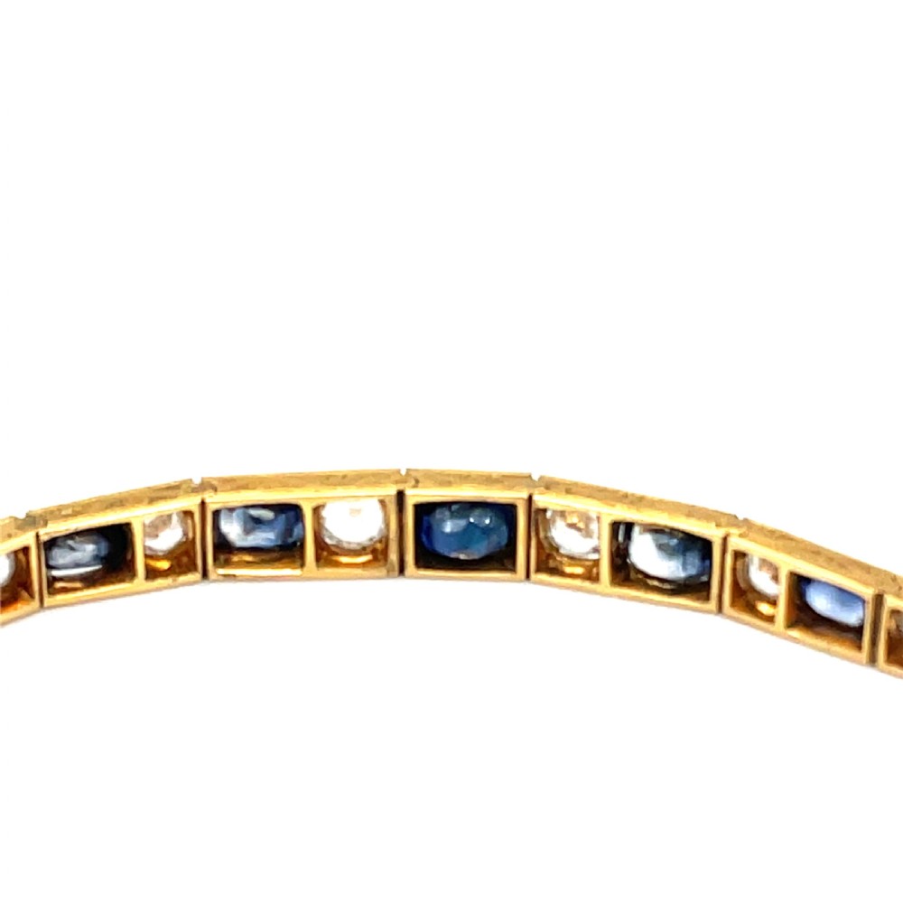 An Edwardian 9ct gold link bracelet featuring alternating set blue sapphires and clear round gemstones in articulated rectangular panels. View III