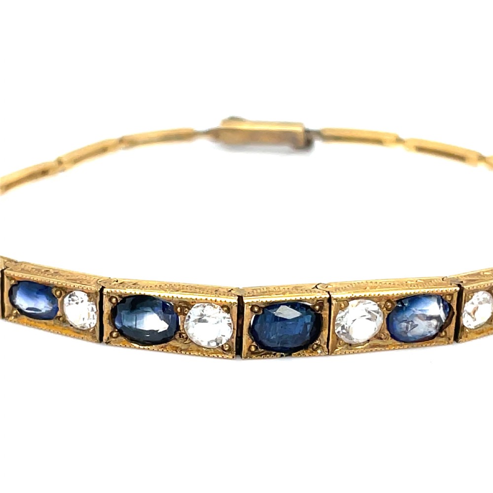 An Edwardian 9ct gold link bracelet featuring alternating set blue sapphires and clear round gemstones in articulated rectangular panels. View IV
