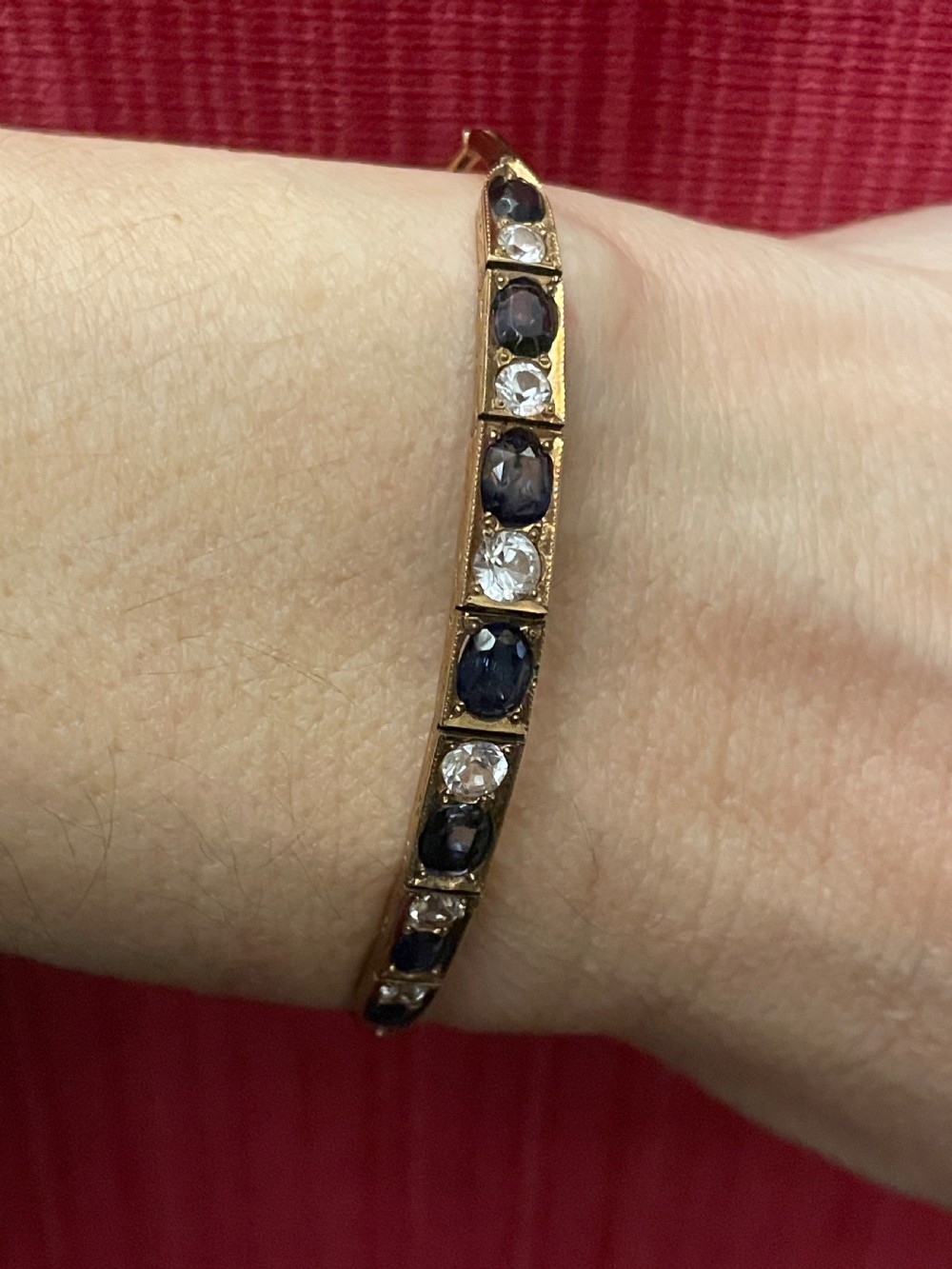 An Edwardian 9ct gold link bracelet featuring alternating set blue sapphires and clear round gemstones in articulated rectangular panels. View V