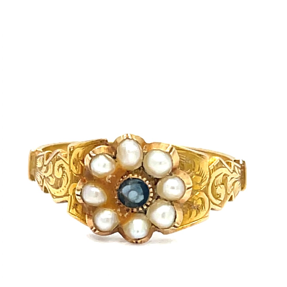 A Victorian 9ct gold mourning ring featuring a central blue agate surrounded by a floral cluster of seed pearls on an engraved gold band.