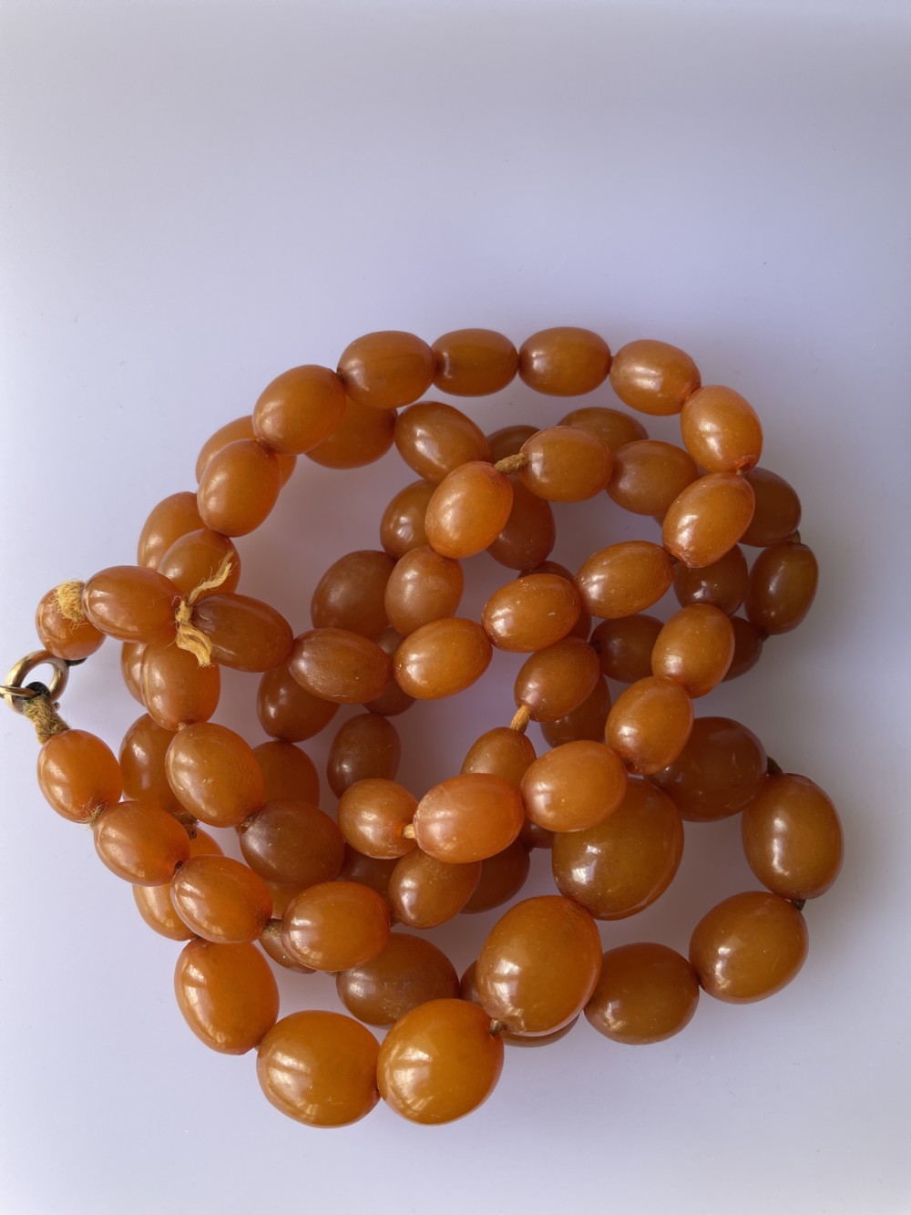 A strand of polished, oval-shaped natural Baltic amber beads in warm honey tones with a metal clasp. View IV