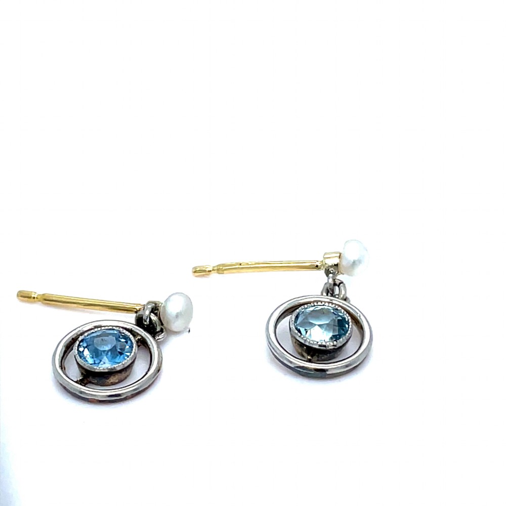 A pair of Edwardian drop earrings featuring round bezel-set aquamarine gemstones inside open circular mounts suspended from pearl studs. View VI