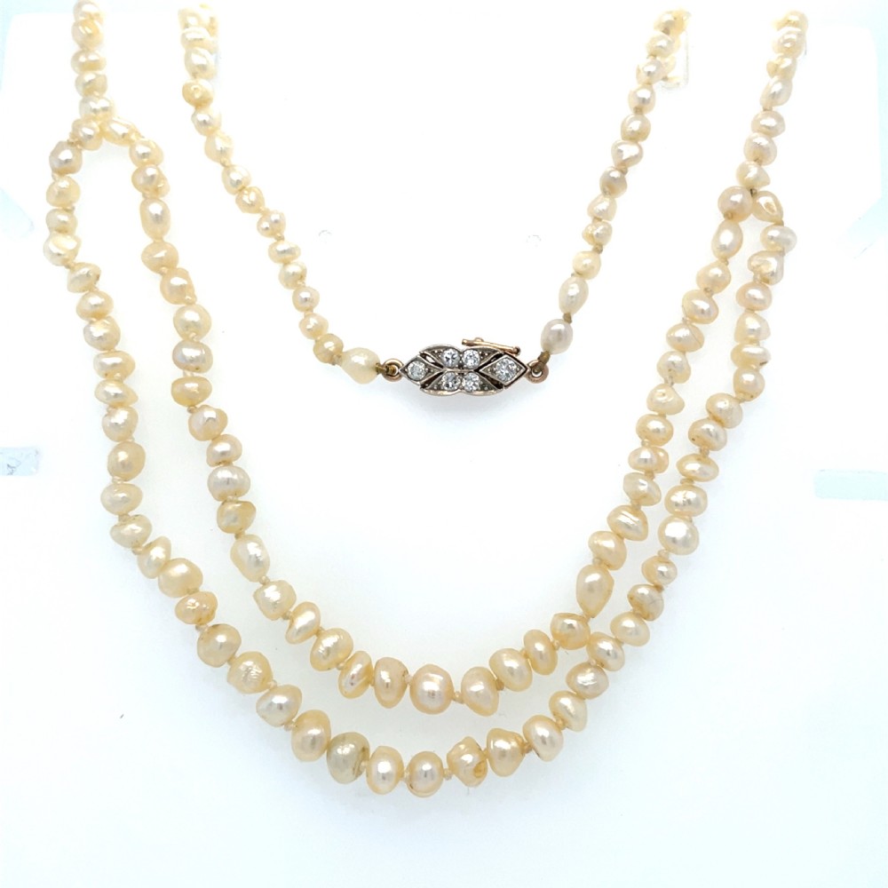 An antique double strand of natural cream pearls connected with an ornate geometric diamond-set clasp.