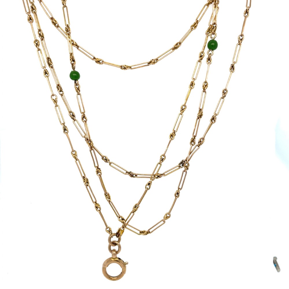 An Edwardian 9ct yellow gold longuard chain featuring elongated links, twisted wire connectors, green gemstone beads, and a circular bolt ring fastener.