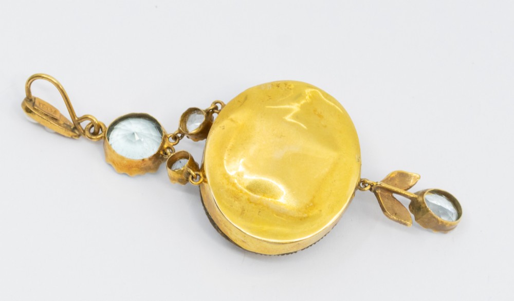 A Victorian gold pendant featuring a large oval rock crystal bordered by split seed pearls, flanked by pale blue aquamarine stones and leaf motifs. View VI