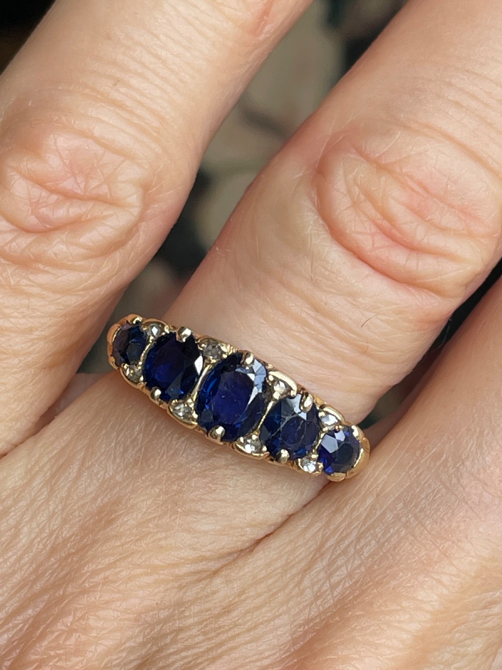 A Victorian 18ct yellow gold boat ring set with five graduated oval blue sapphires and small diamond accents. View IV