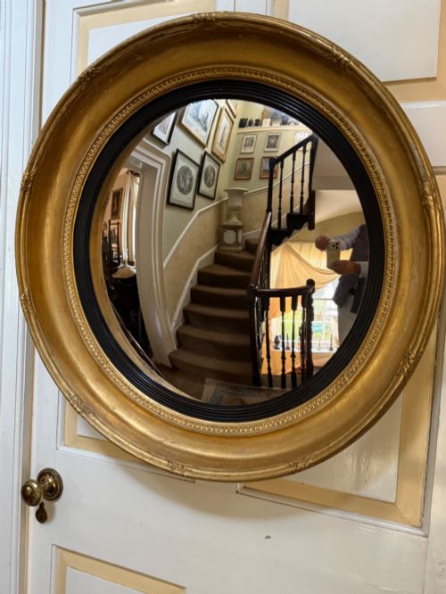 fig 1. A circular early 19th-century Regency convex mirror featuring a gilded carved frame with an ebonised inner reeded slip.
