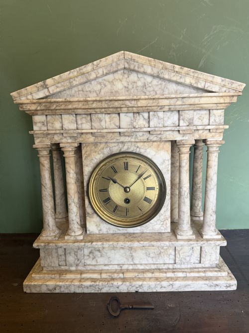 fig 1. A late nineteenth-century carved cream alabaster mantel clock styled as a classical Greek temple with columns and a central brass dial.