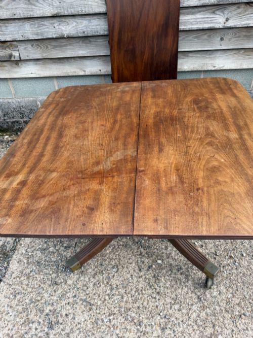 fig 1. An early nineteenth-century mahogany extending dining table featuring a central reeded pedestal base with brass castors and an extra extension leaf standing behind.