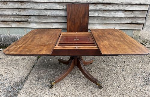 fig 2. An early nineteenth-century mahogany extending dining table featuring a central reeded pedestal base with brass castors and an extra extension leaf standing behind.