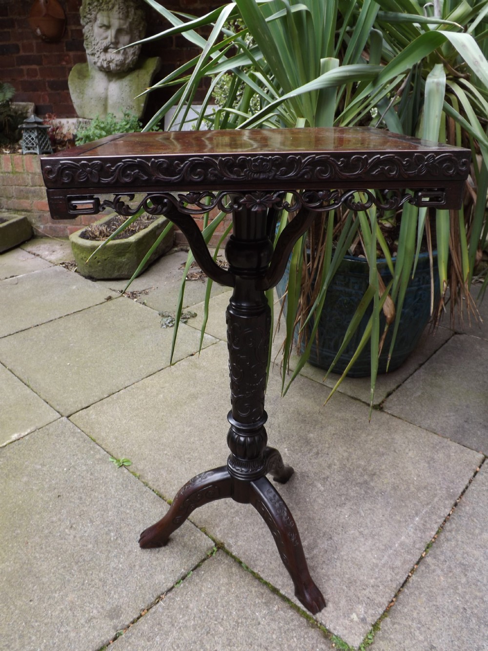 A late 19th-century Chinese dark hardwood tripod table featuring an intricately carved square top, turned pedestal column, and three carved splayed legs.
