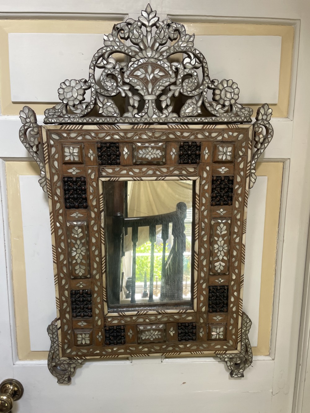 An antique Levantine walnut wall mirror featuring hand-carved decorative cresting and elaborate geometric mother-of-pearl and bone inlay.