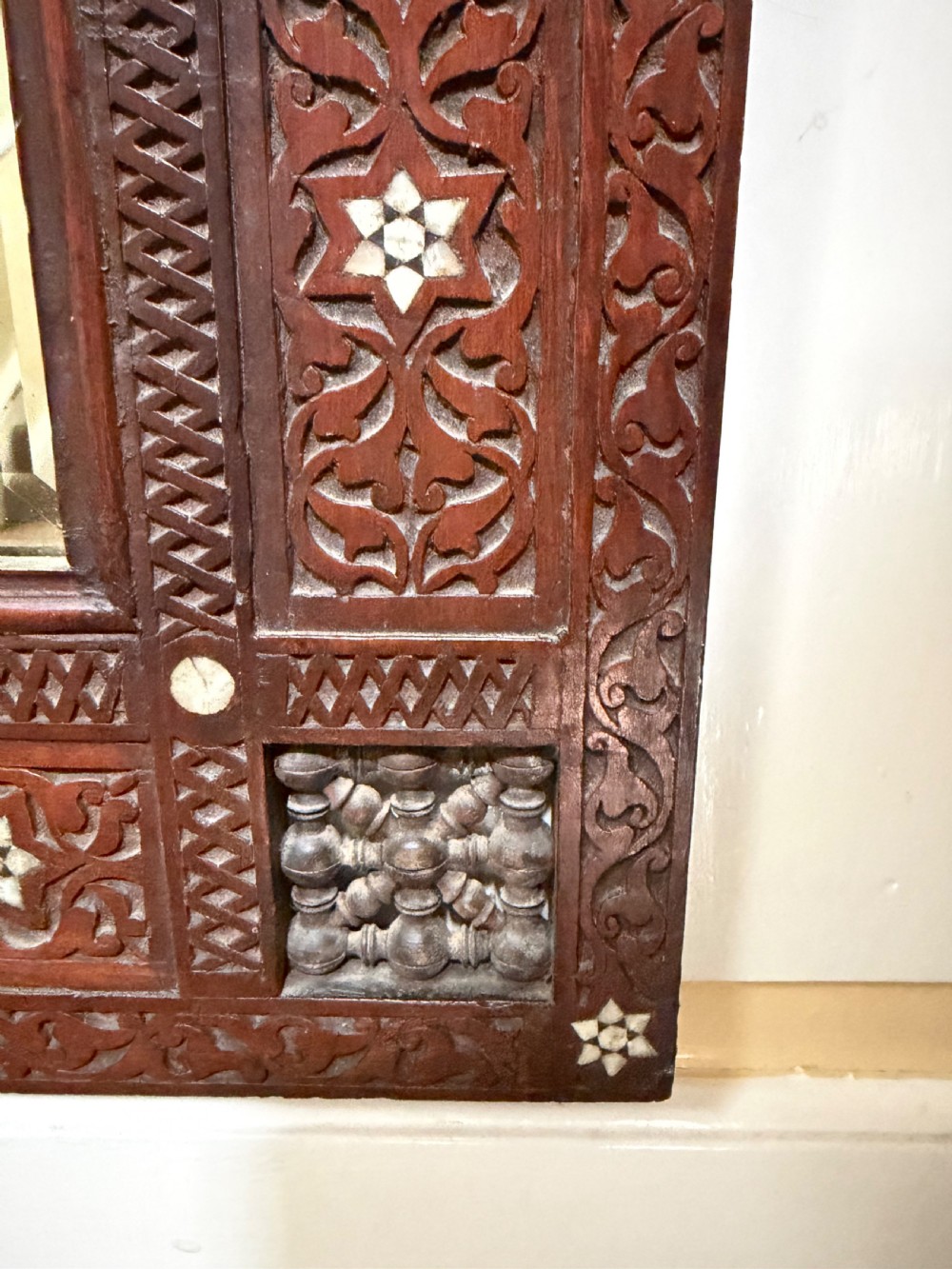 A late nineteenth-century carved dark wood wall mirror featuring geometric mother-of-pearl inlay, mashrabiya turned panels, and a shaped cresting. View III