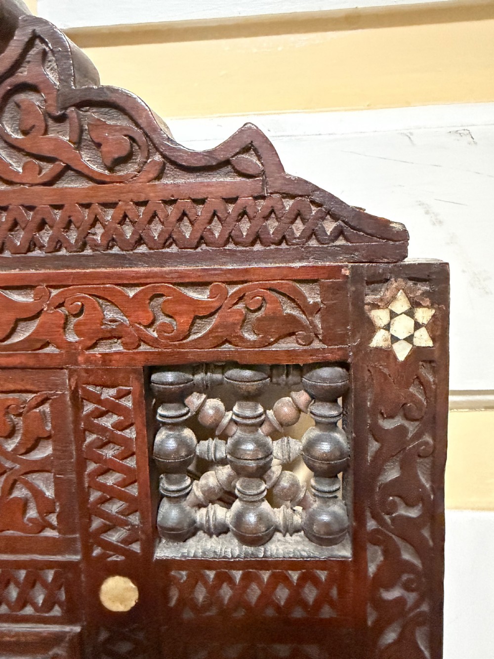 A late nineteenth-century carved dark wood wall mirror featuring geometric mother-of-pearl inlay, mashrabiya turned panels, and a shaped cresting. View IV