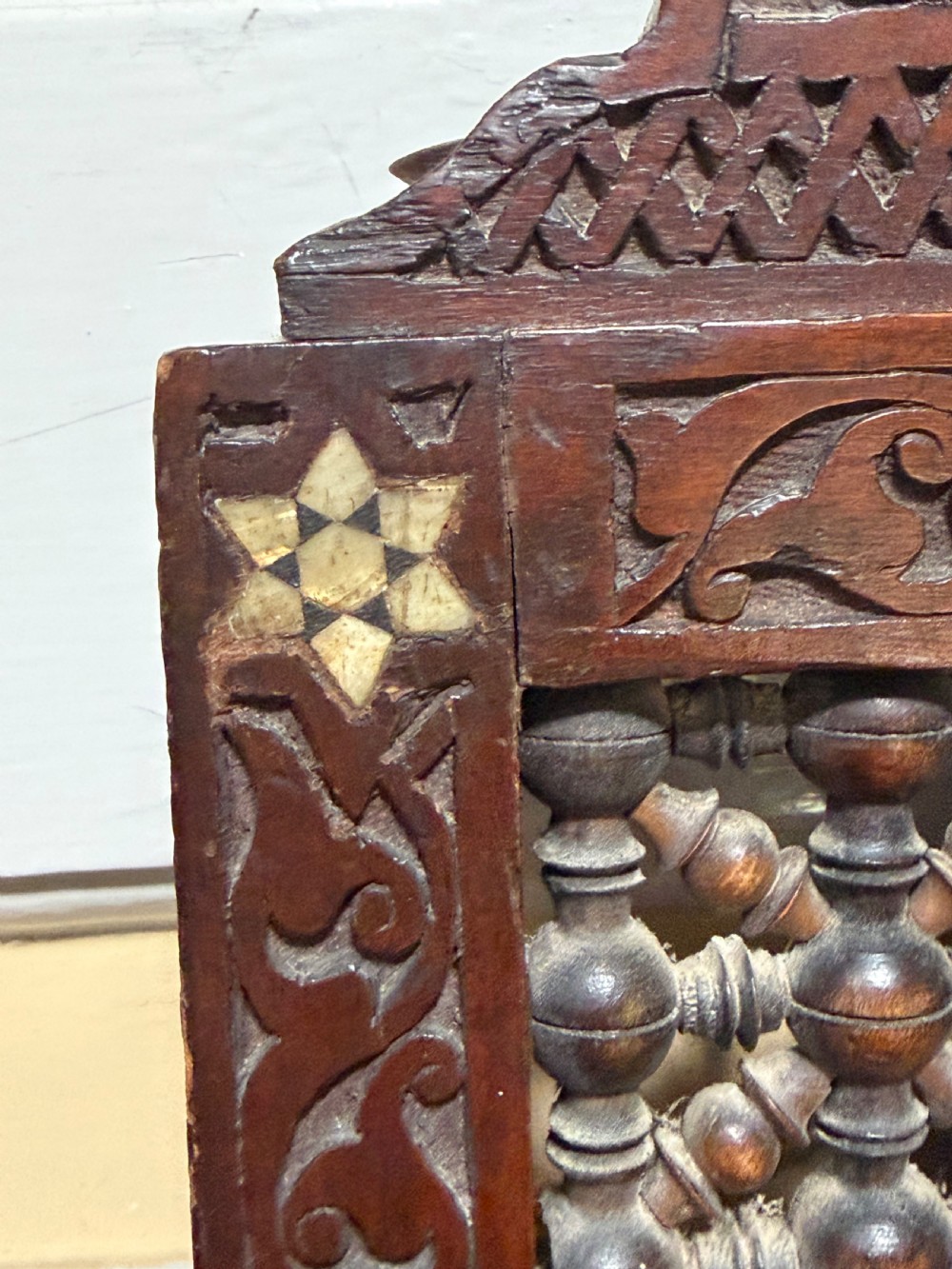 A late nineteenth-century carved dark wood wall mirror featuring geometric mother-of-pearl inlay, mashrabiya turned panels, and a shaped cresting. View VI