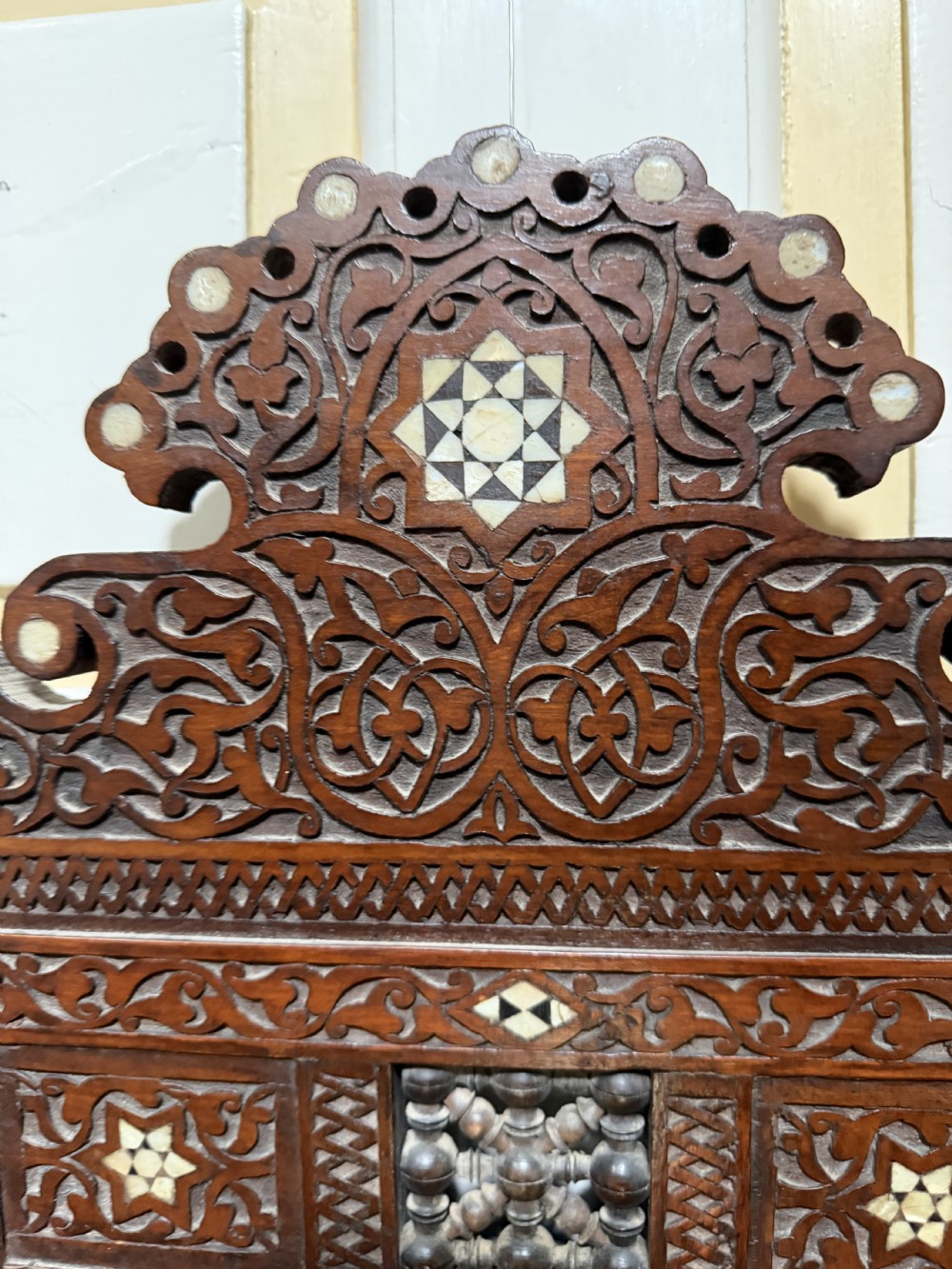 A late nineteenth-century carved dark wood wall mirror featuring geometric mother-of-pearl inlay, mashrabiya turned panels, and a shaped cresting. View VII