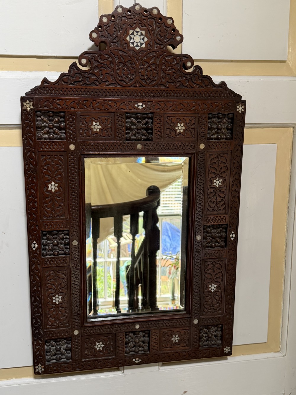 A late nineteenth-century carved dark wood wall mirror featuring geometric mother-of-pearl inlay, mashrabiya turned panels, and a shaped cresting. View VIII