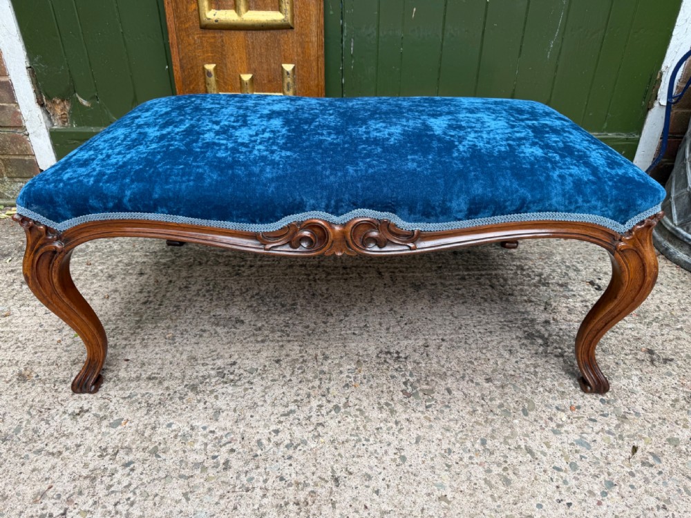 A mid-19th-century centre stool featuring carved walnut cabriole legs, carved aprons, and blue velvet upholstered top.