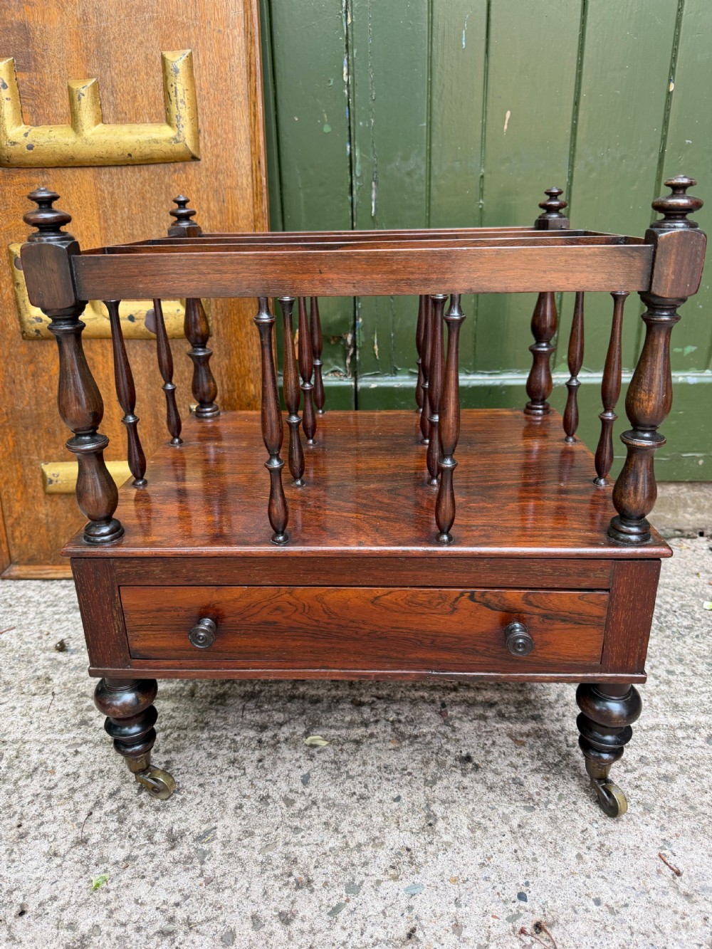 An early nineteenth-century George IV rosewood music canterbury featuring turned spindle divisions, a single base drawer, turned legs, and brass castors.