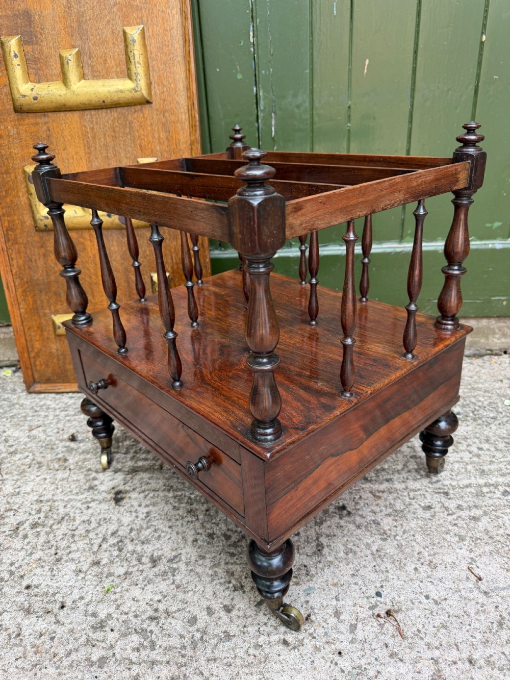 An early nineteenth-century George IV rosewood music canterbury featuring turned spindle divisions, a single base drawer, turned legs, and brass castors. View IV