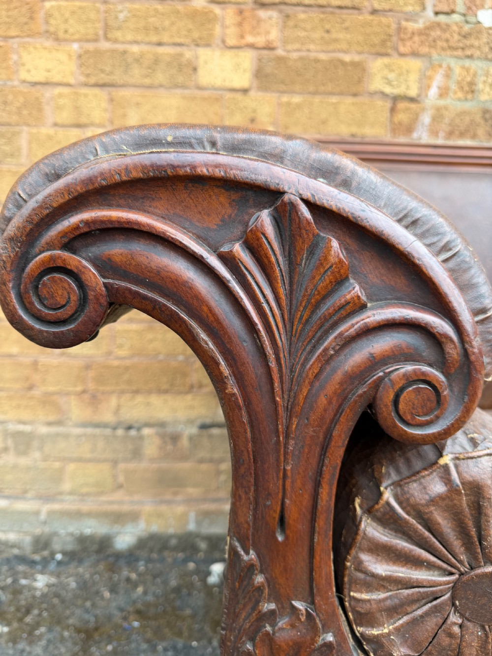 An early nineteenth-century William IV mahogany framed settee with worn brown leather upholstery, carved scroll arms, turned legs on brass castors, and matching bolster cushions. View VI