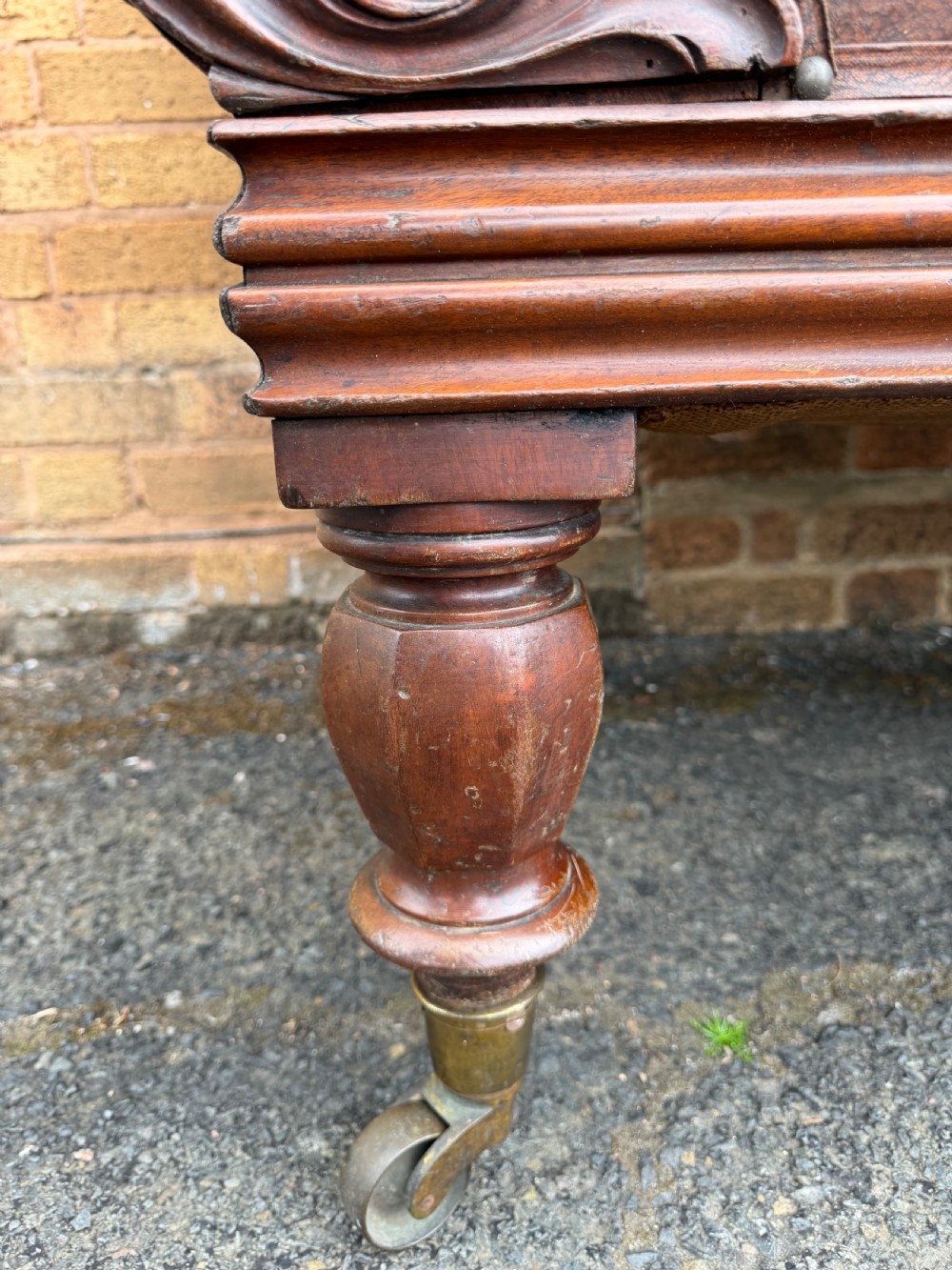 An early nineteenth-century William IV mahogany framed settee with worn brown leather upholstery, carved scroll arms, turned legs on brass castors, and matching bolster cushions. View VII