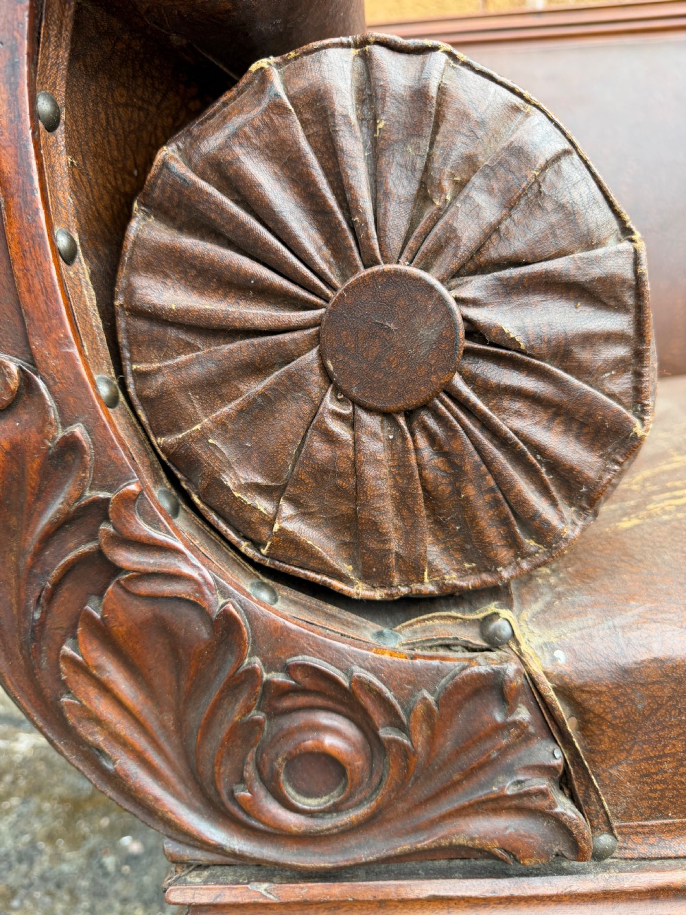 An early nineteenth-century William IV mahogany framed settee with worn brown leather upholstery, carved scroll arms, turned legs on brass castors, and matching bolster cushions. View IX
