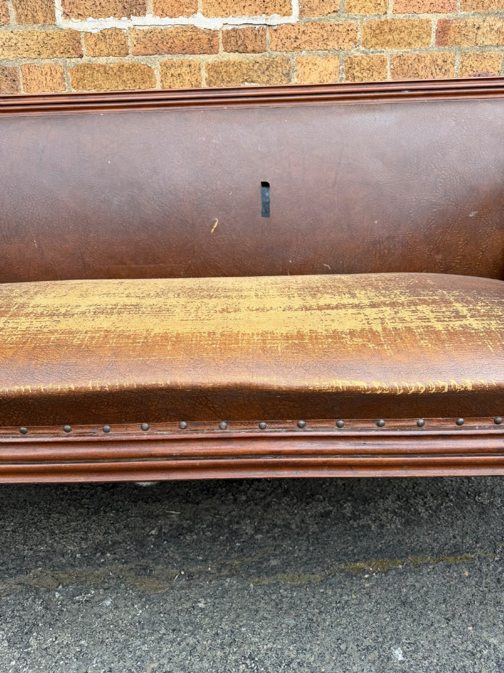 An early nineteenth-century William IV mahogany framed settee with worn brown leather upholstery, carved scroll arms, turned legs on brass castors, and matching bolster cushions. View XII