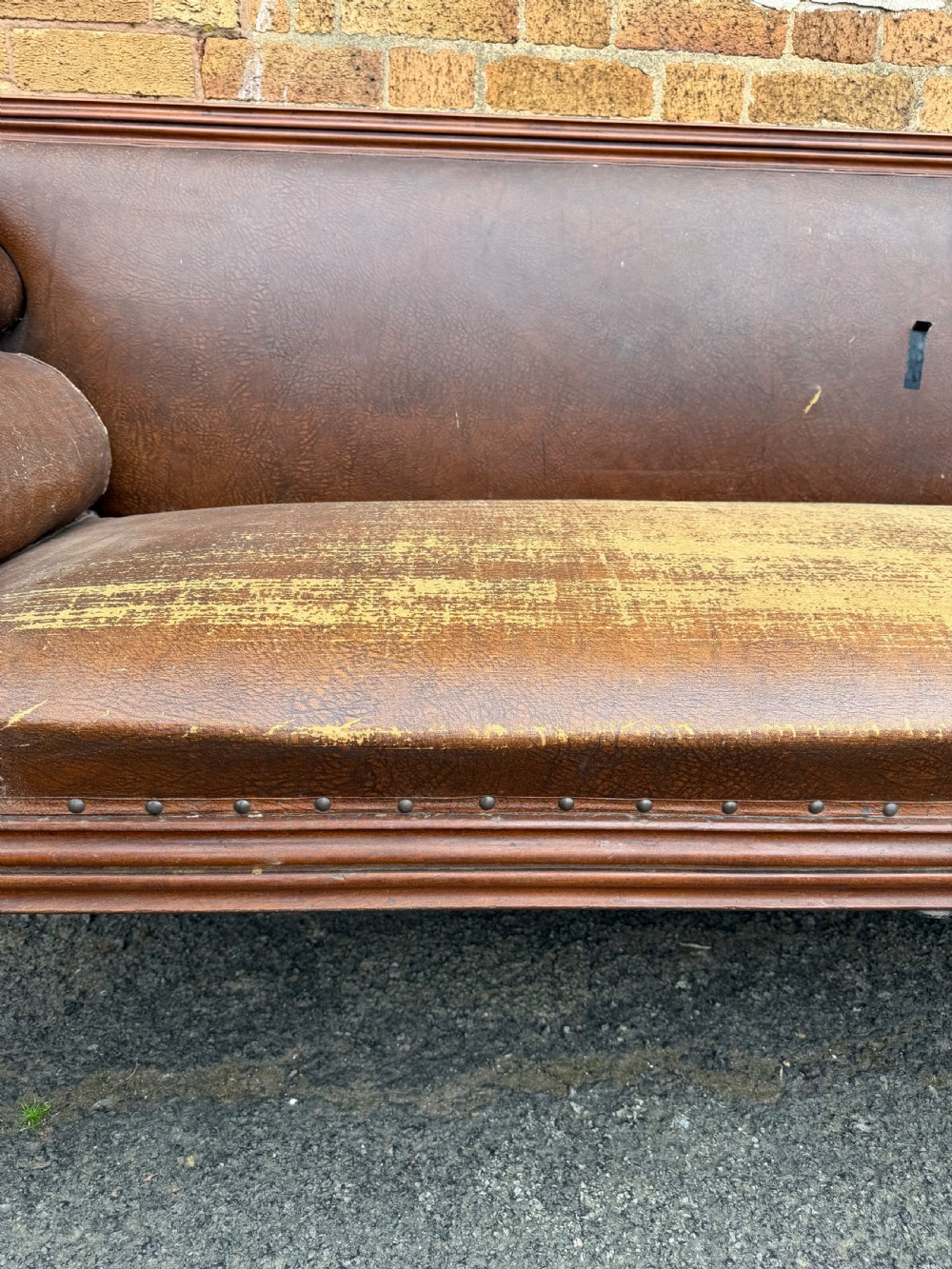 An early nineteenth-century William IV mahogany framed settee with worn brown leather upholstery, carved scroll arms, turned legs on brass castors, and matching bolster cushions. View XIII