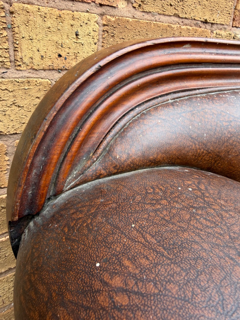 An early nineteenth-century William IV mahogany framed settee with worn brown leather upholstery, carved scroll arms, turned legs on brass castors, and matching bolster cushions. View XVII