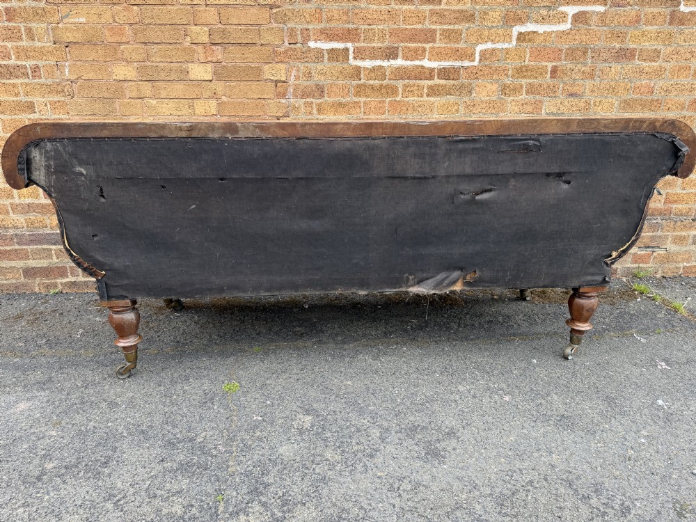 An early nineteenth-century William IV mahogany framed settee with worn brown leather upholstery, carved scroll arms, turned legs on brass castors, and matching bolster cushions. View XXII