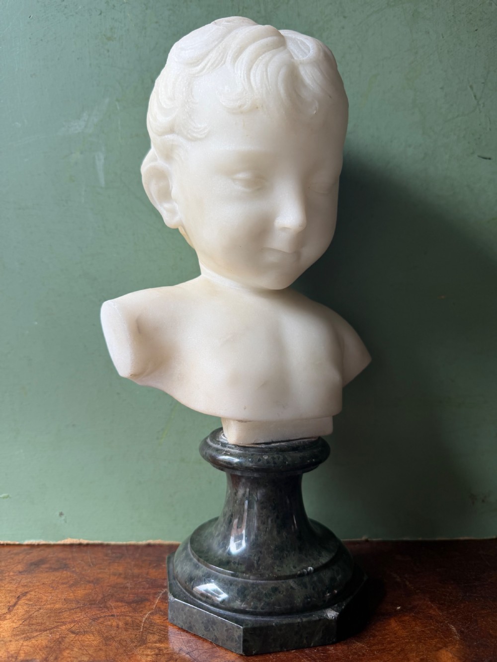 A late nineteenth-century white marble bust of a young boy set upon a dark green turned marble socle base. View XVI