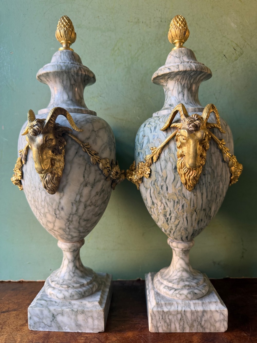 A pair of late 19th-century French Louis XVI style Campan vert marble urns adorned with gilt bronze ram head handles, floral swags, and pinecone finials. View IV