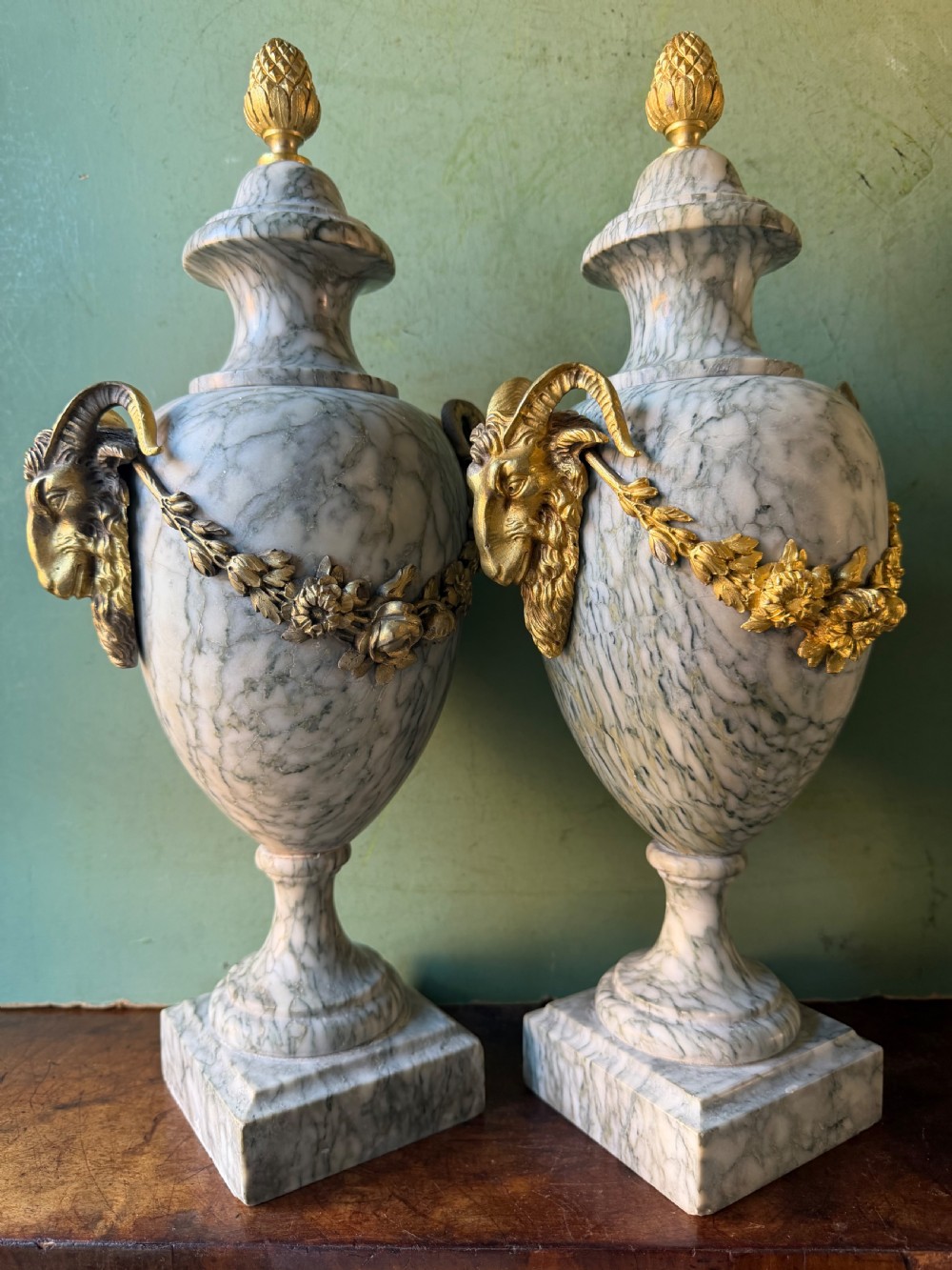 A pair of late 19th-century French Louis XVI style Campan vert marble urns adorned with gilt bronze ram head handles, floral swags, and pinecone finials. View VI