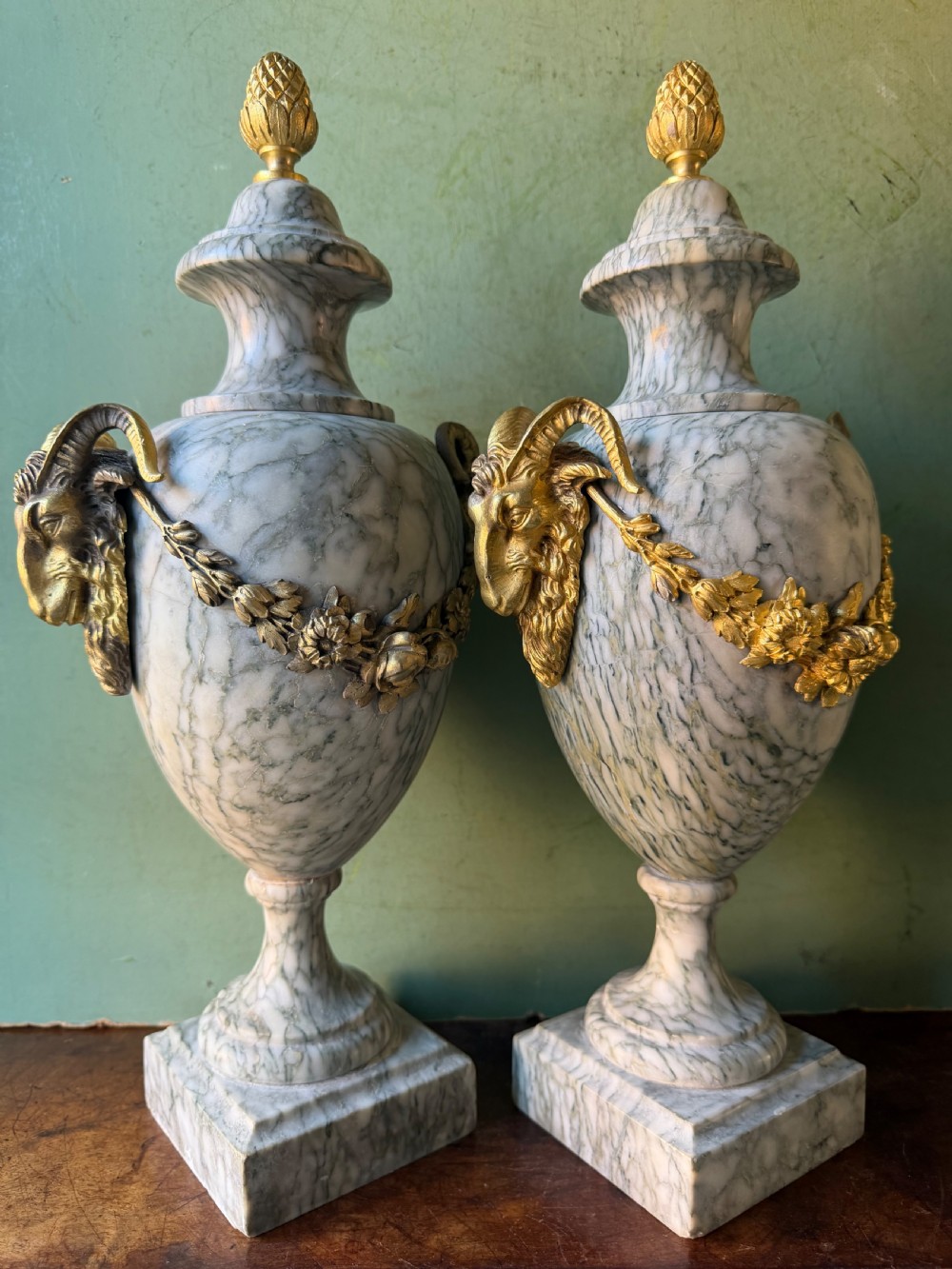 A pair of late 19th-century French Louis XVI style Campan vert marble urns adorned with gilt bronze ram head handles, floral swags, and pinecone finials. View VII