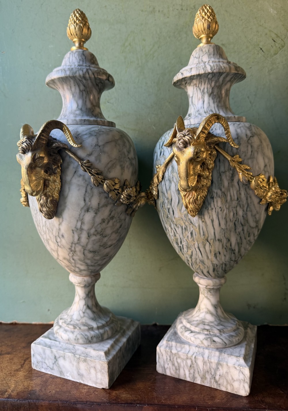 A pair of late 19th-century French Louis XVI style Campan vert marble urns adorned with gilt bronze ram head handles, floral swags, and pinecone finials. View VIII